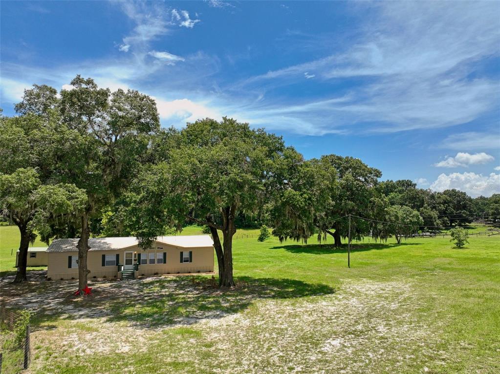 A tan manufactured home sits on a grassy lot shaded by several large oak trees — 18546 NE 5TH TERRACE ROAD, CITRA, FL