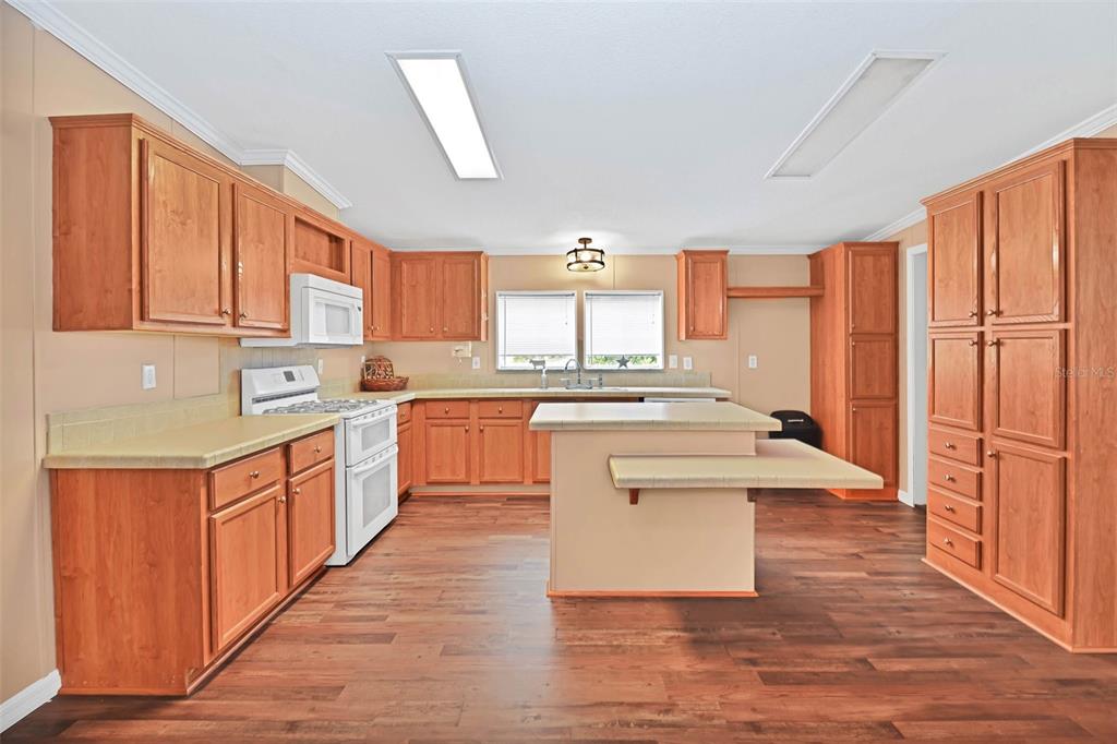 A kitchen with wood cabinets, a central island, white appliances, and wood-look flooring — 18546 NE 5TH TERRACE ROAD, CITRA, FL
