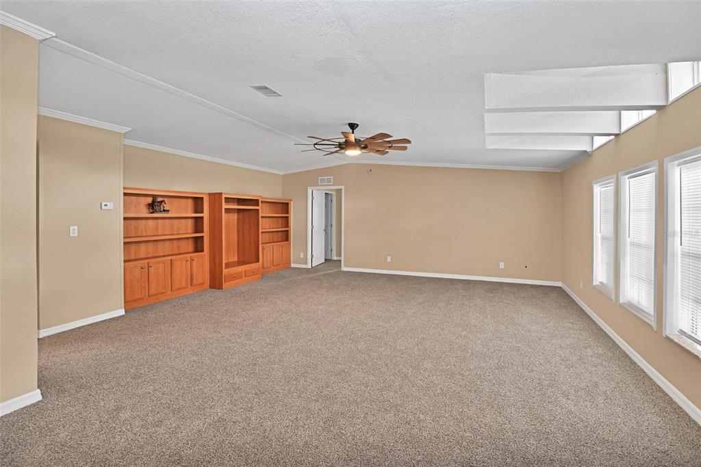 A spacious living room features beige walls, tan carpeting, a ceiling fan, and built-in shelving — 18546 NE 5TH TERRACE ROAD, CITRA, FL