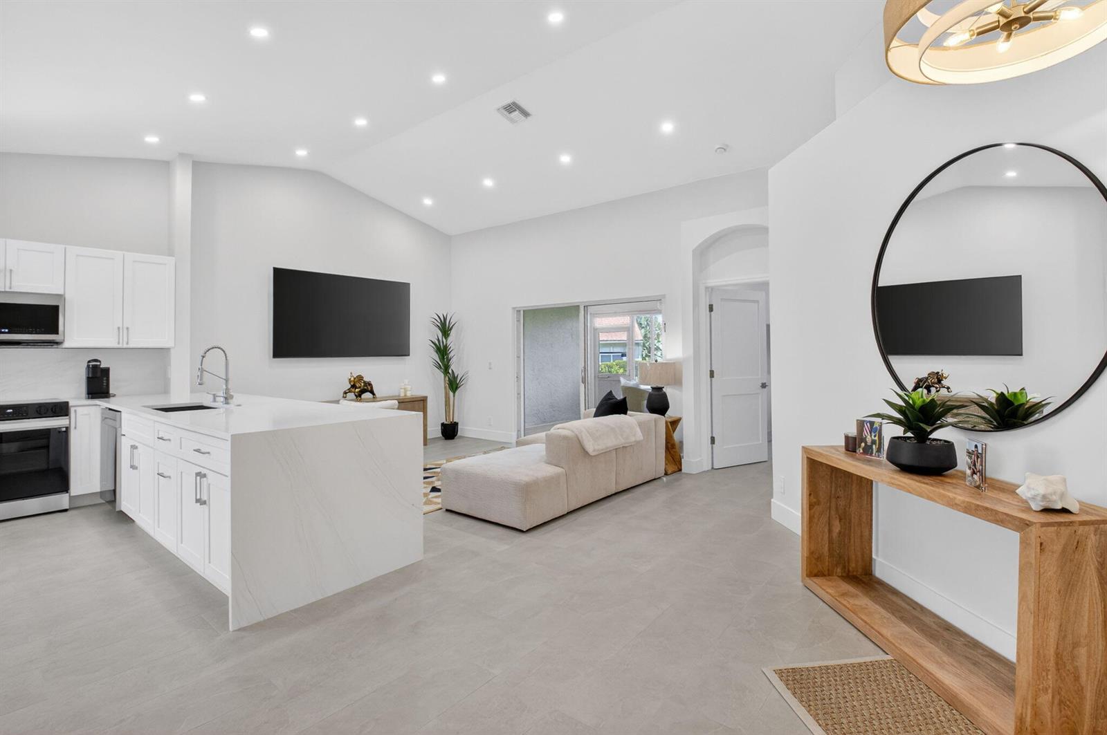 A modern open-concept kitchen and living area with white cabinetry, a stone island, and tile flooring — 6171 Floral Lakes Drive, Delray Beach FL 33484, DELRAY BEACH, FL