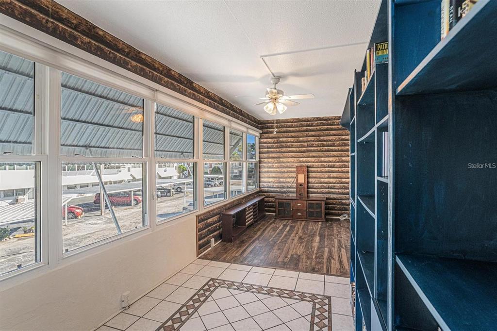A sunroom features log-style walls, a ceiling fan, tile flooring, and a large blue bookshelf — 1900 59TH AVENUE N UNIT 210, ST PETERSBURG, FL