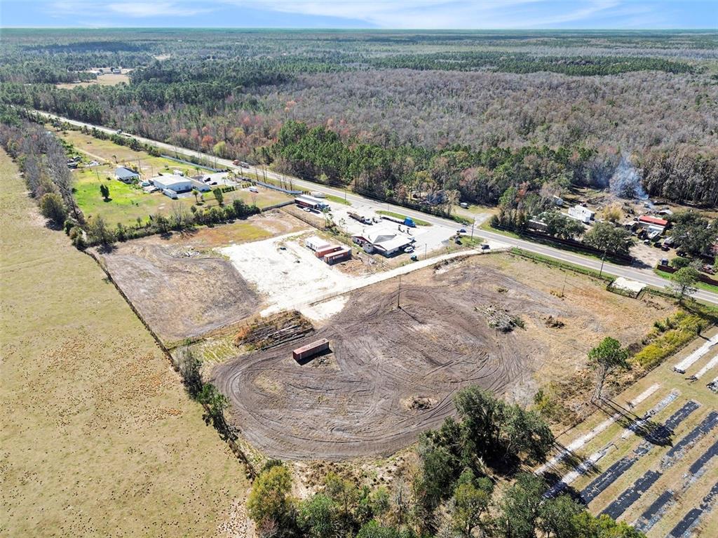 An aerial view shows a cleared commercial lot with a shipping container and nearby buildings — 3824 STATE ROAD 33, CLERMONT, FL