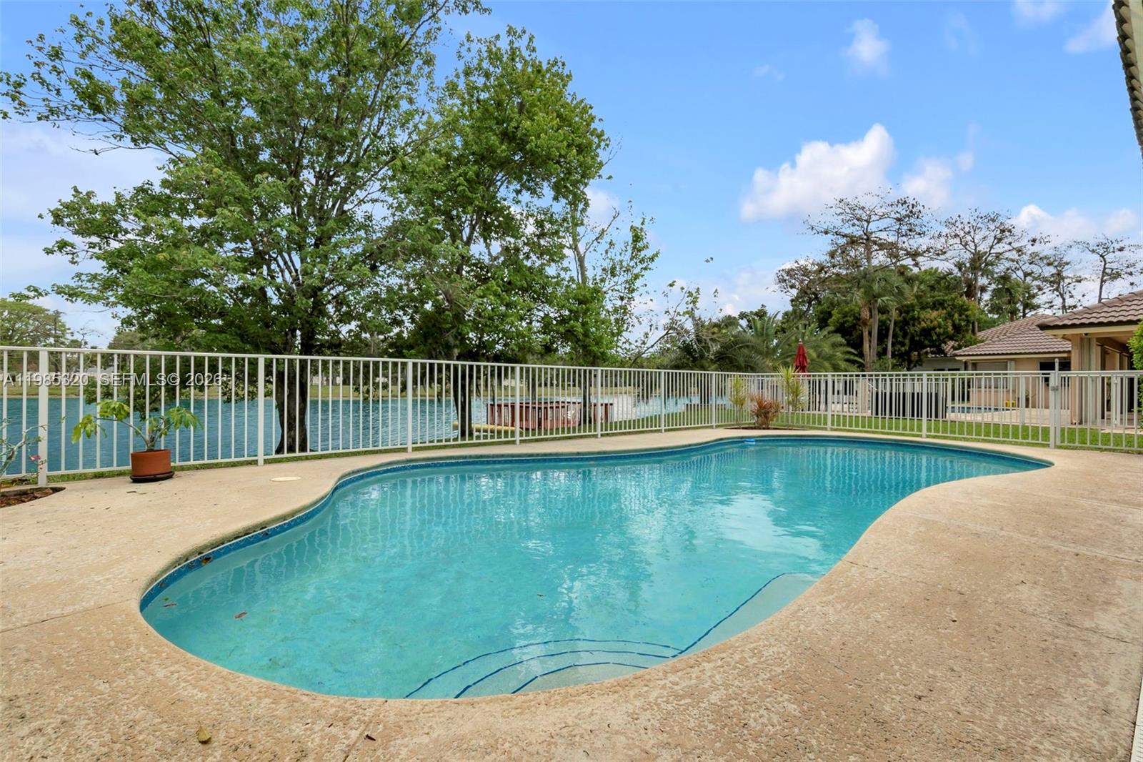 A swimming pool sits on a patio enclosed by a white fence overlooking a lake — 4927 NW 67th Ave, Lauderhill FL 33319, LAUDERHILL, FL