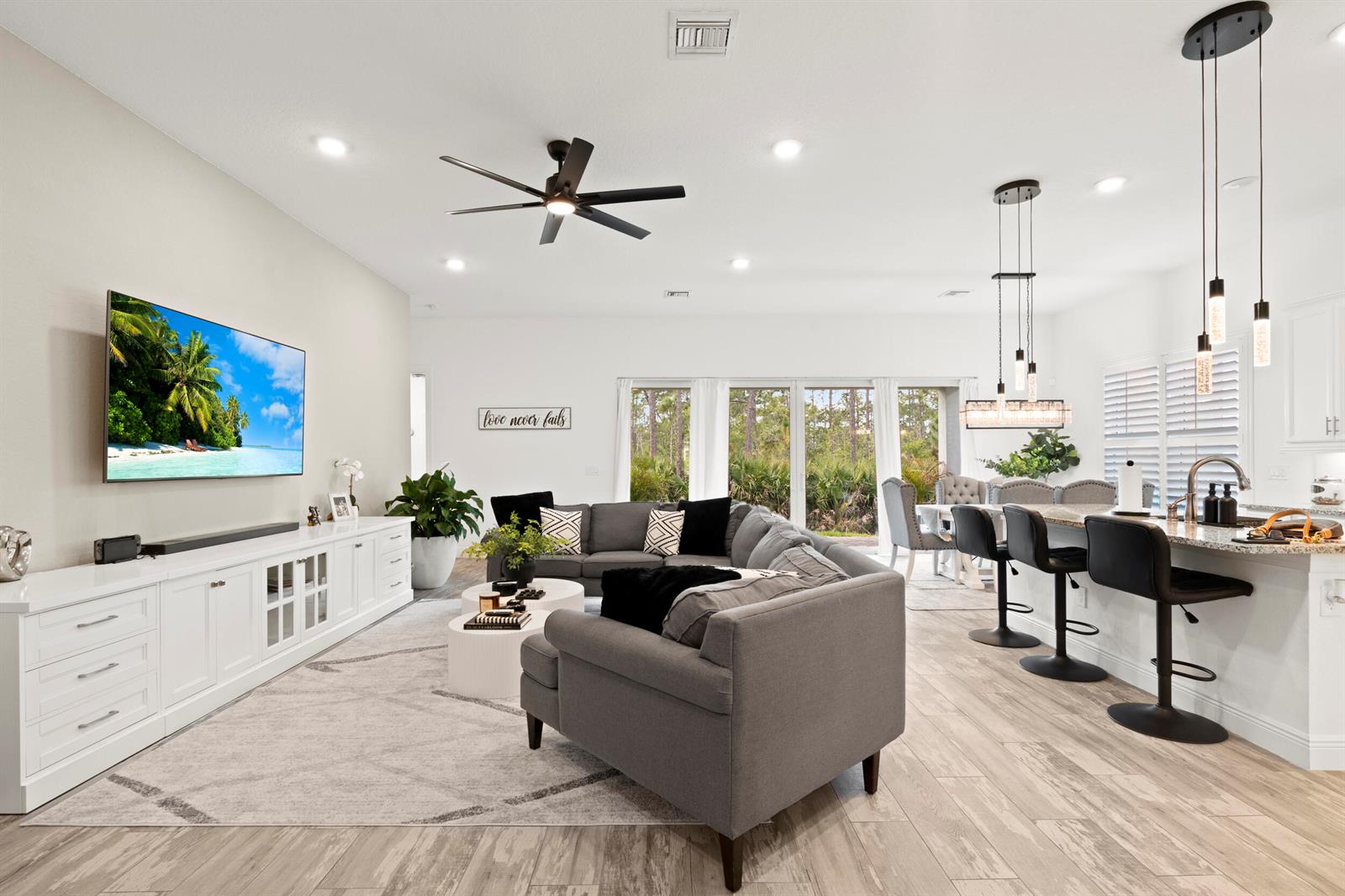 An open-concept living room features a grey sectional sofa, white media console, and kitchen island — 4630 SW Ardsley Drive, Stuart FL 34997, STUART, FL