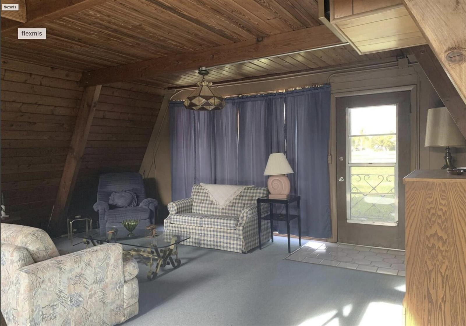 A living room with wood-paneled slanted walls, a blue carpet, and a glass-paned exterior door — 31110 U.s. 441, Okeechobee FL 34972, OKEECHOBEE, FL