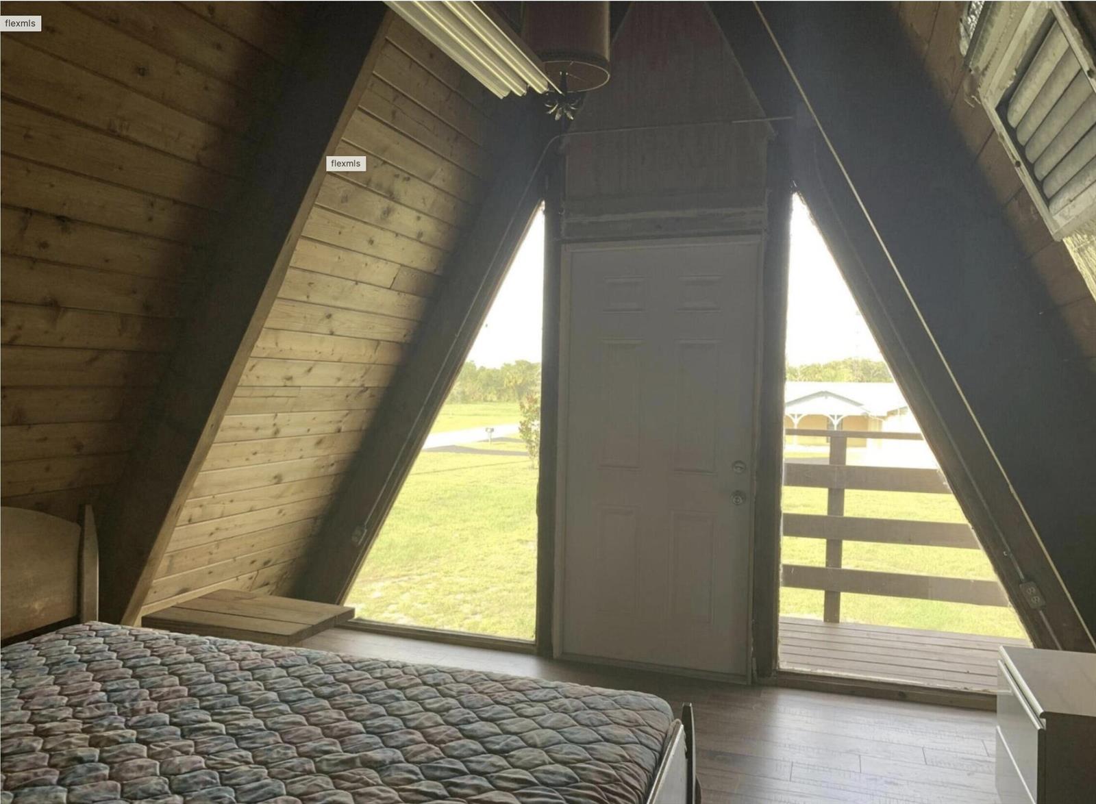 A bedroom in an A-frame house with wood-paneled walls, a bed, and a balcony door — 31110 U.s. 441, Okeechobee FL 34972, OKEECHOBEE, FL