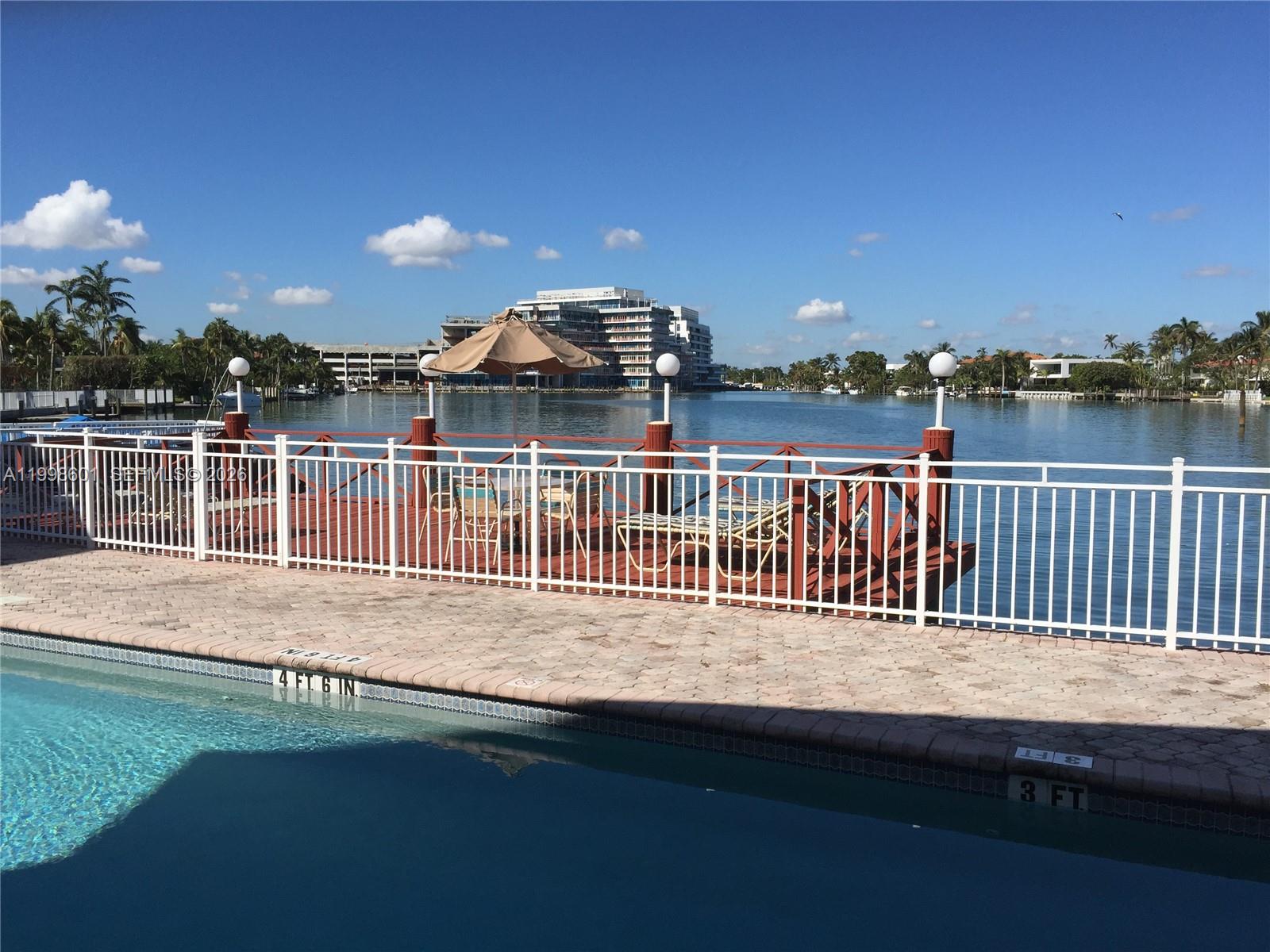 A swimming pool sits in front of a fenced deck overlooking a calm waterway — 4740 Pine Tree Dr # 26, Miami Beach FL 33140, MIAMI BEACH, FL