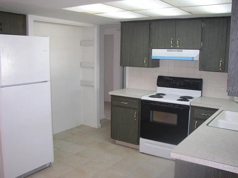 A kitchen features dark wood cabinets, white appliances, a tiled floor, and a drop ceiling — 7907 YUCCA DRIVE, NEW PORT RICHEY, FL