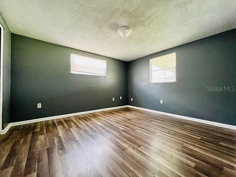 An empty bedroom features dark gray walls, wood-look flooring, and two windows with blinds — 7907 YUCCA DRIVE, NEW PORT RICHEY, FL