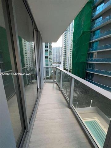 A balcony with glass railings overlooks a swimming pool and nearby high-rise buildings — 77 SE 5th St # 1704, Miami FL 33131, MIAMI, FL