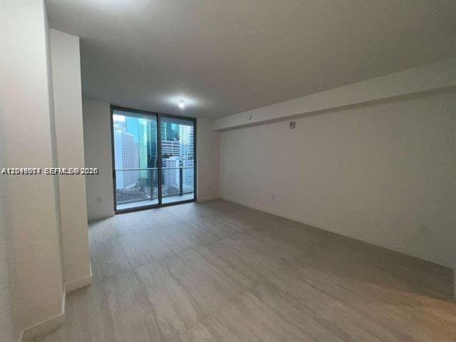 An empty room features light-colored tile flooring, white walls, and a large glass balcony door — 77 SE 5th St # 1704, Miami FL 33131, MIAMI, FL