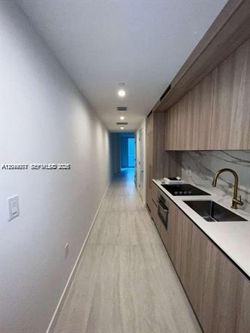 A narrow galley kitchen features light wood cabinetry, white countertops, and a stainless steel sink — 77 SE 5th St # 1704, Miami FL 33131, MIAMI, FL