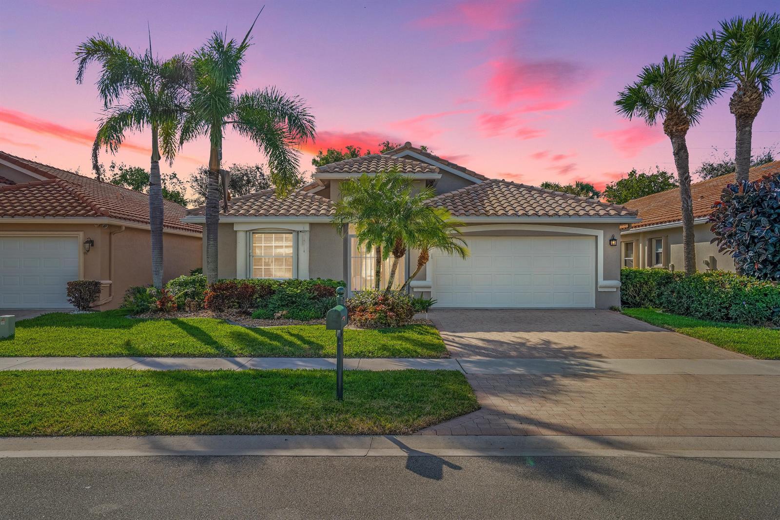 A single-story suburban house with a tile roof, two-car garage, and palm trees at sunset — 7348 Trentino Way, Boynton Beach FL 33472, BOYNTON BEACH, FL