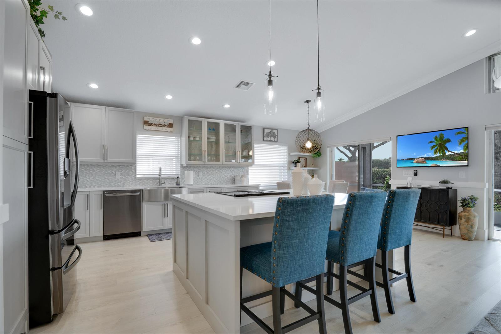 A modern kitchen features a large white island, blue bar stools, and stainless steel appliances — 7348 Trentino Way, Boynton Beach FL 33472, BOYNTON BEACH, FL