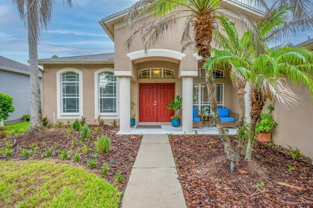 A tan house exterior features a red double front door, columns, and a palm tree — 16135 BRIDGEDALE DRIVE, LITHIA, FL