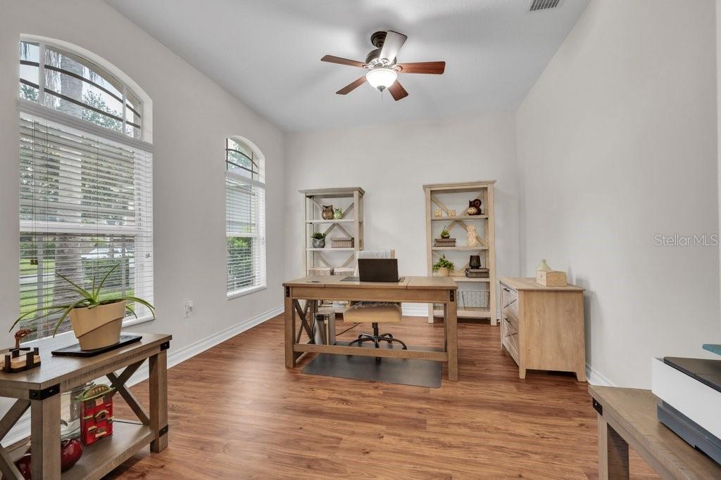 A home office with wood-look flooring, a desk, two bookshelves, and large arched windows — 16135 BRIDGEDALE DRIVE, LITHIA, FL