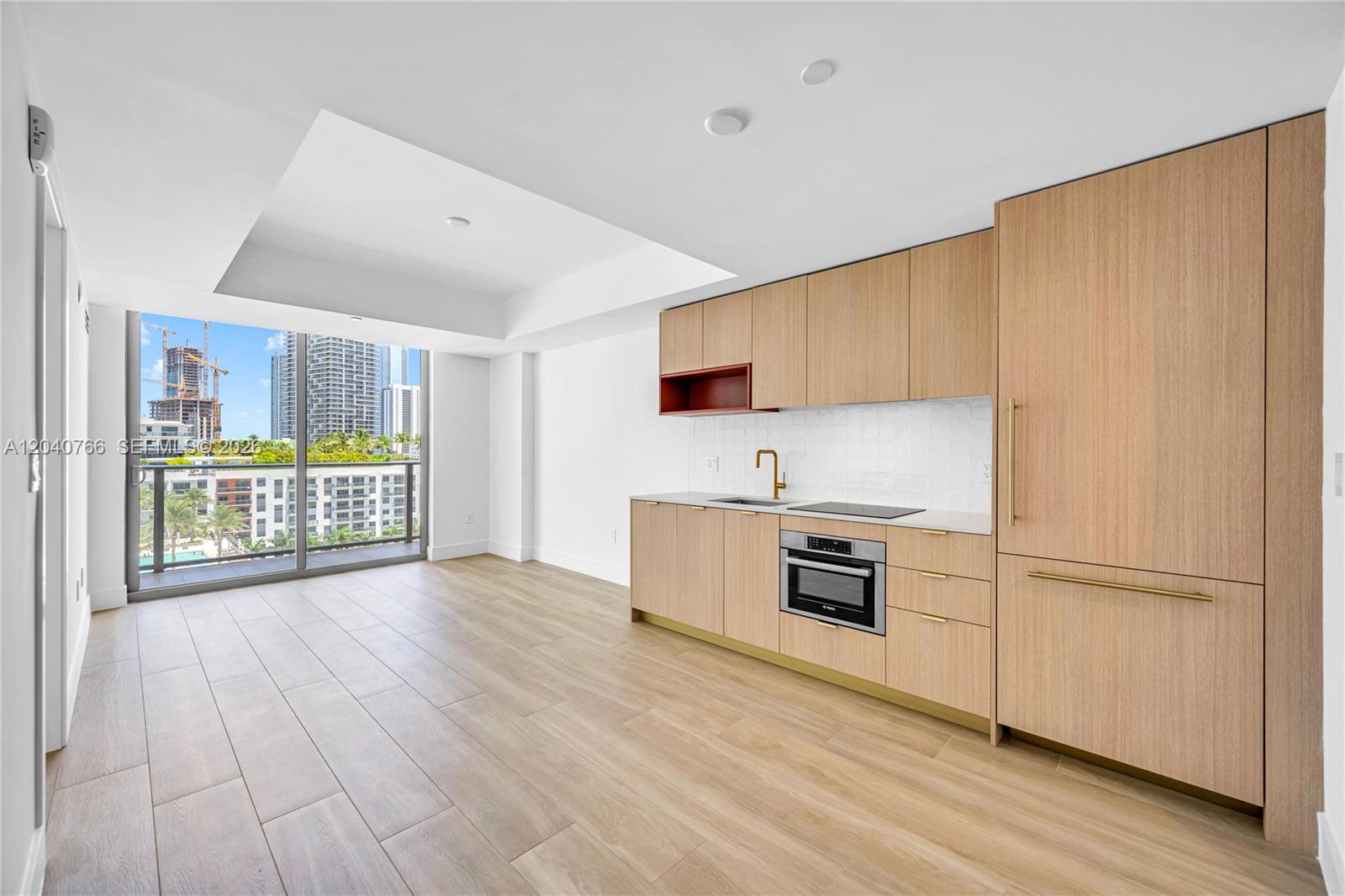 A modern kitchen features light wood cabinetry, gold hardware, and a balcony with city views — 90 NE 32nd, Miami FL 33127, MIAMI, FL