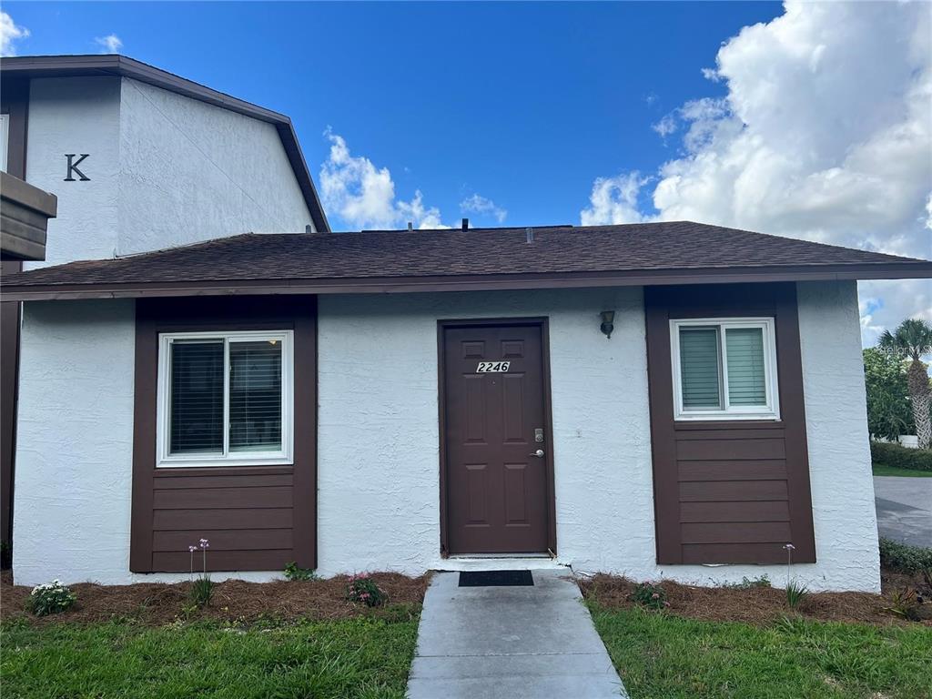 The exterior of a single-story residential unit features white stucco walls, brown trim, and a brown door — 39132 COUNTY ROAD 54 UNIT 2246, ZEPHYRHILLS, FL
