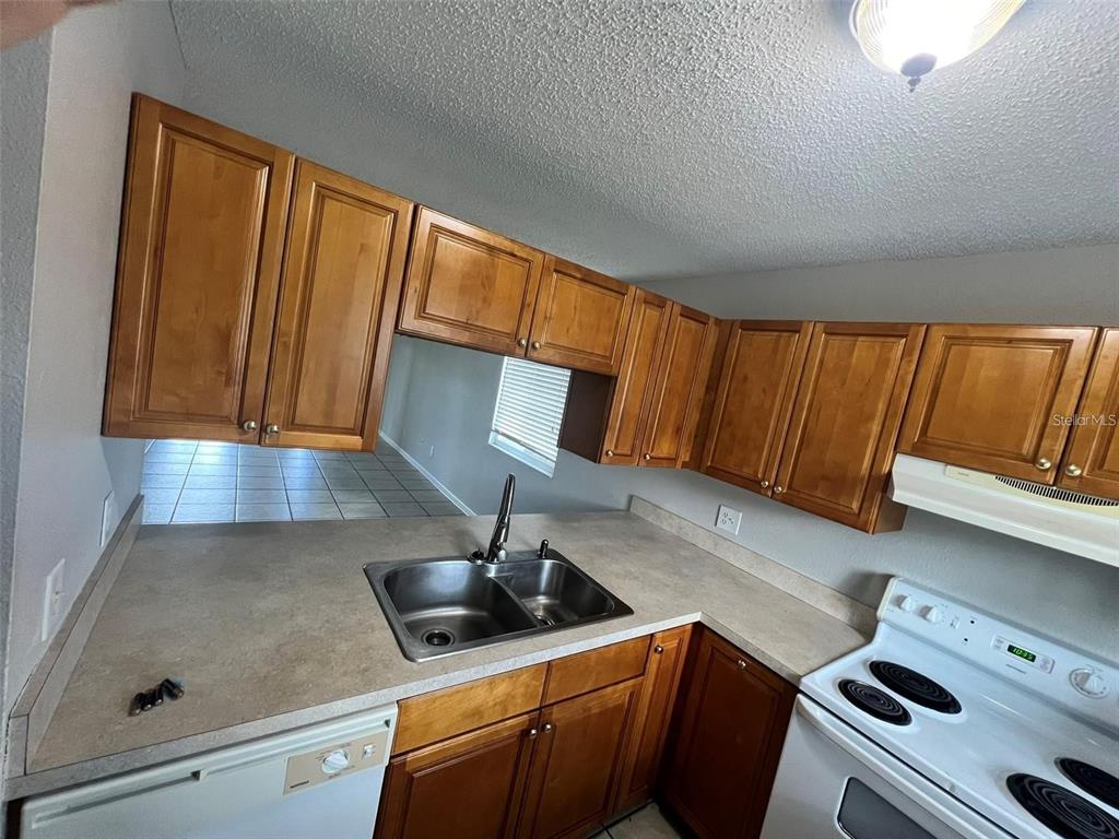 A kitchen features wood cabinets, laminate countertops, a double sink, and a white electric stove — 39132 COUNTY ROAD 54 UNIT 2246, ZEPHYRHILLS, FL