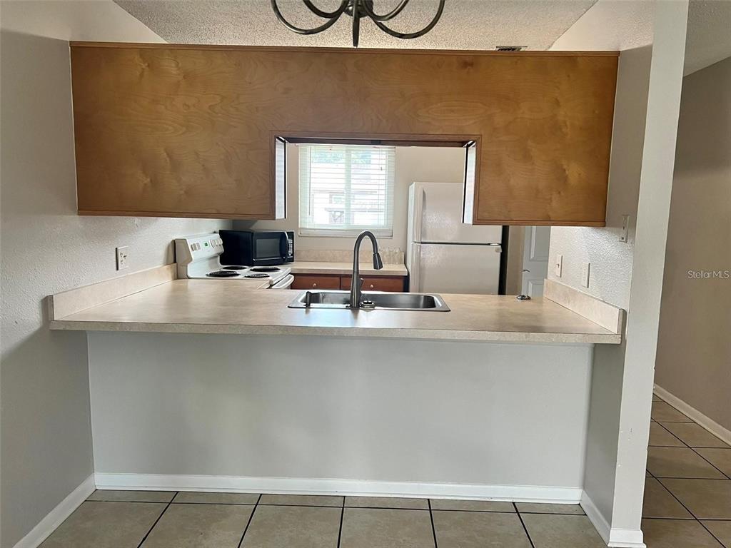 A kitchen features a pass-through window, laminate countertops, light wood cabinets, and tile flooring — 39132 COUNTY ROAD 54 UNIT 2246, ZEPHYRHILLS, FL
