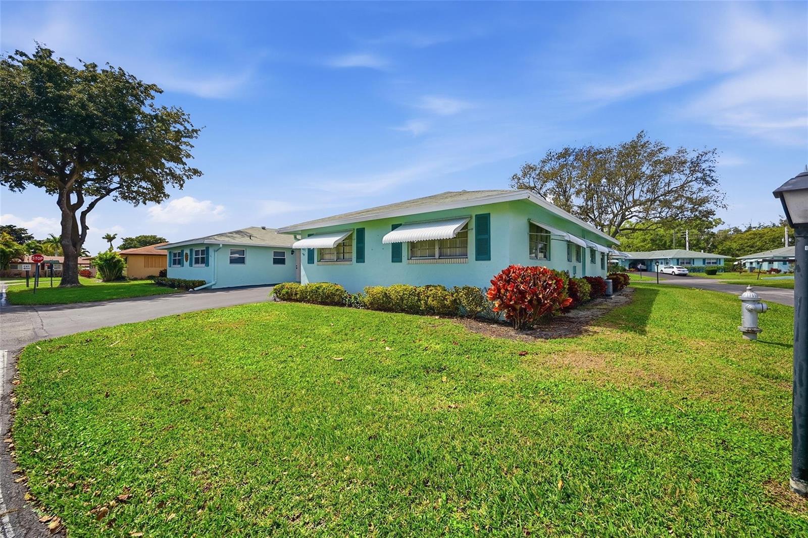 A light green single-story house with white awnings sits on a grassy corner lot — 602 Hummingbird Lane # 602, Delray Beach FL 33445, DELRAY BEACH, FL