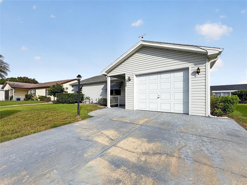 A single-story house with light gray siding, a white garage door, and a concrete driveway — 1222 SANTOS PLACE, LADY LAKE, FL