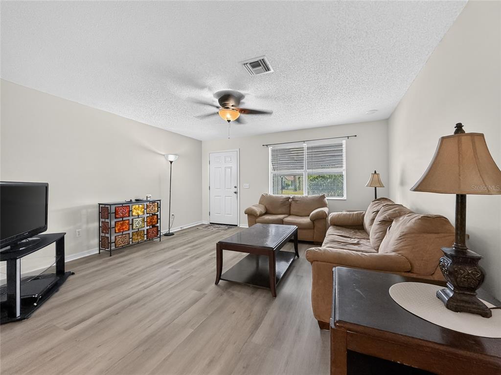 A living room features light wood-look flooring, beige walls, a ceiling fan, and two sofas — 1222 SANTOS PLACE, LADY LAKE, FL