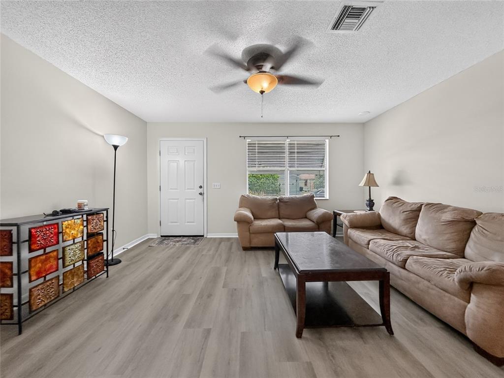 A living room features light wood-look flooring, a ceiling fan, and tan upholstered furniture — 1222 SANTOS PLACE, LADY LAKE, FL
