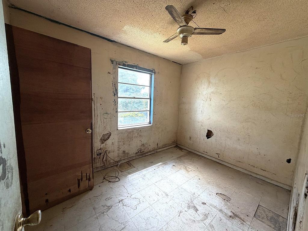 A small, dilapidated bedroom features a ceiling fan, a single window, and damaged wall surfaces — 14741 12TH STREET, DADE CITY, FL