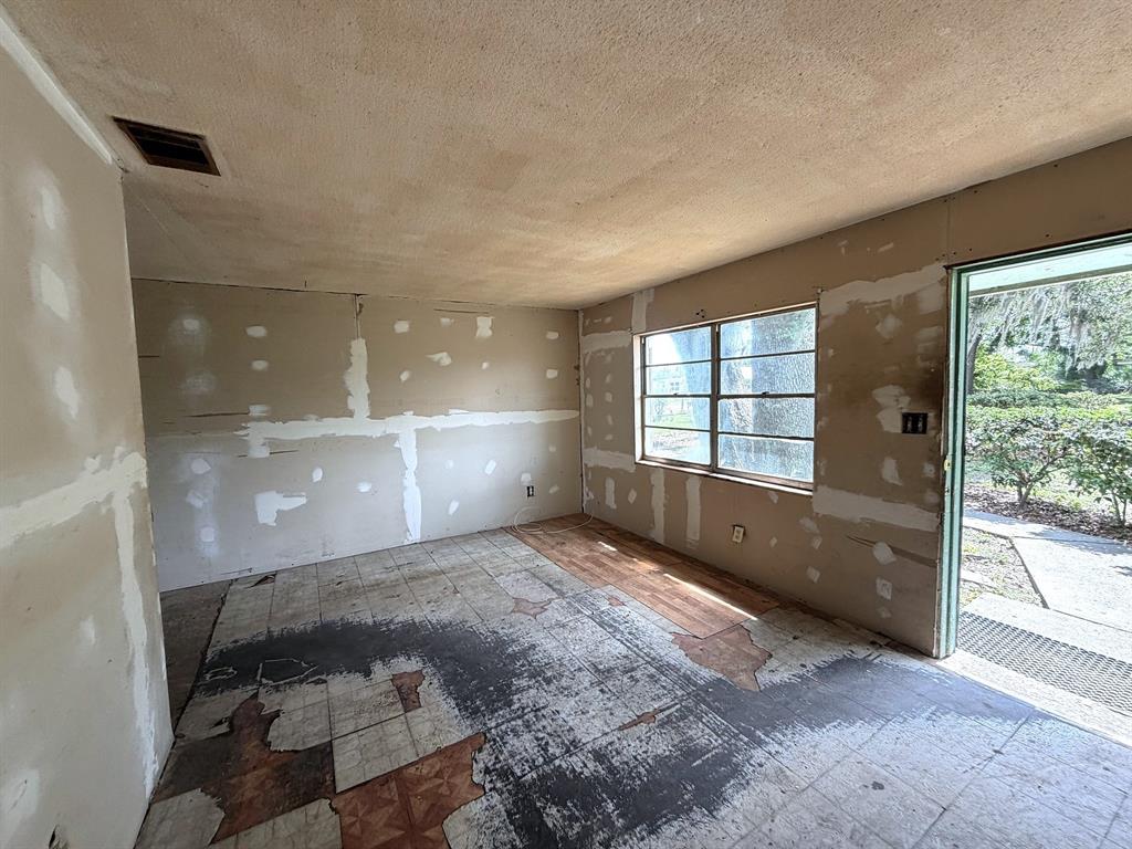 An unfinished room features exposed drywall, a textured ceiling, and worn, partially removed floor tiles — 14741 12TH STREET, DADE CITY, FL