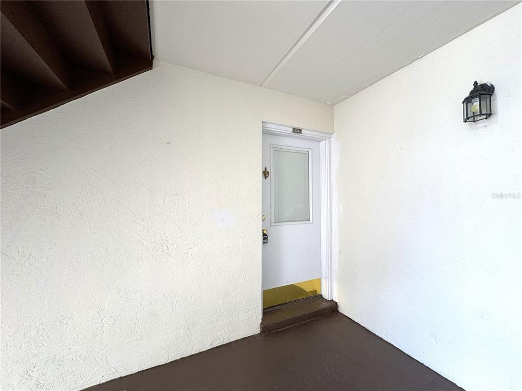 A white exterior door with a window is set in a plain wall near stairs — 2400 FOREST DRIVE UNIT 139, INVERNESS, FL