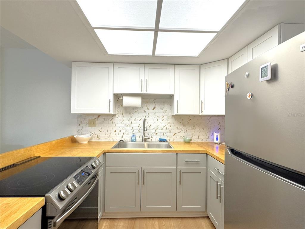 A kitchen features white upper cabinets, gray lower cabinets, wood countertops, and a stainless refrigerator — 2400 FOREST DRIVE UNIT 139, INVERNESS, FL