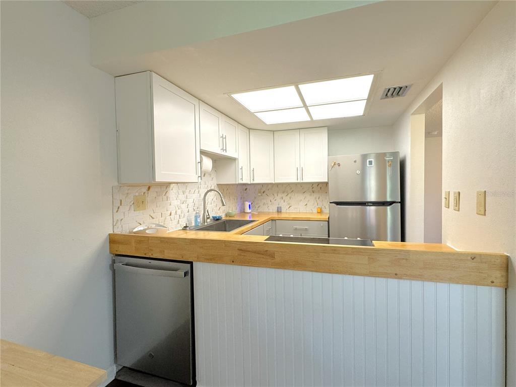 A kitchen features white cabinets, a wood countertop, stainless steel appliances, and a tiled backsplash — 2400 FOREST DRIVE UNIT 139, INVERNESS, FL