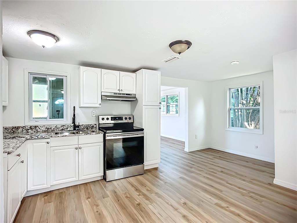 A kitchen features white cabinets, granite countertops, stainless steel appliances, and light wood-look flooring — 317 JESSICA STREET S, NOKOMIS, FL
