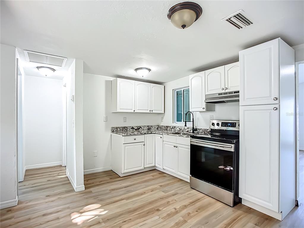 A kitchen features white cabinets, granite countertops, stainless steel appliances, and light wood-look flooring — 317 JESSICA STREET S, NOKOMIS, FL