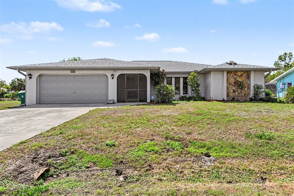 A single-story house with a gray garage, stone accent wall, and a large front yard — 1109 AMPLE AVENUE, PORT CHARLOTTE, FL