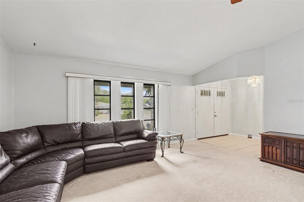 A living room features a large leather sectional, beige carpeting, and a white double-door entrance — 1109 AMPLE AVENUE, PORT CHARLOTTE, FL