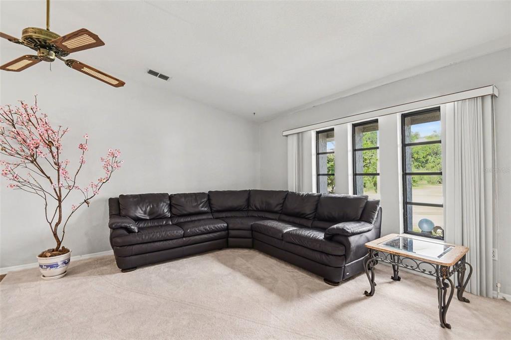 A living room features a large dark leather sectional, a potted tree, and three windows — 1109 AMPLE AVENUE, PORT CHARLOTTE, FL