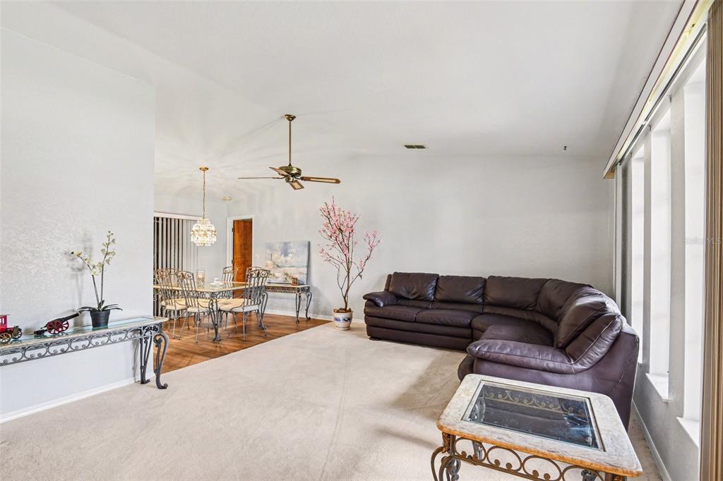 A living room with beige carpet, a dark leather sectional, and an adjacent dining area — 1109 AMPLE AVENUE, PORT CHARLOTTE, FL