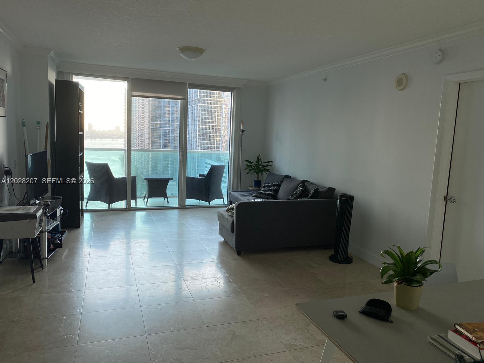 A living room with tile floors, a gray sofa, and a balcony overlooking city buildings — 31 SE 5th St # 2308, Miami FL 33131, MIAMI, FL