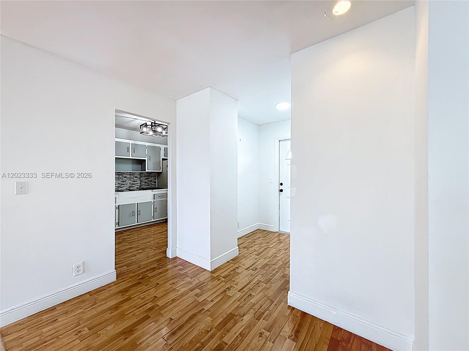 A view of a room with wood-look flooring leading to a kitchen and an entryway — 1000 NE 14th Ave # 411, Hallandale Beach FL 33009, HALLANDALE BEACH, FL