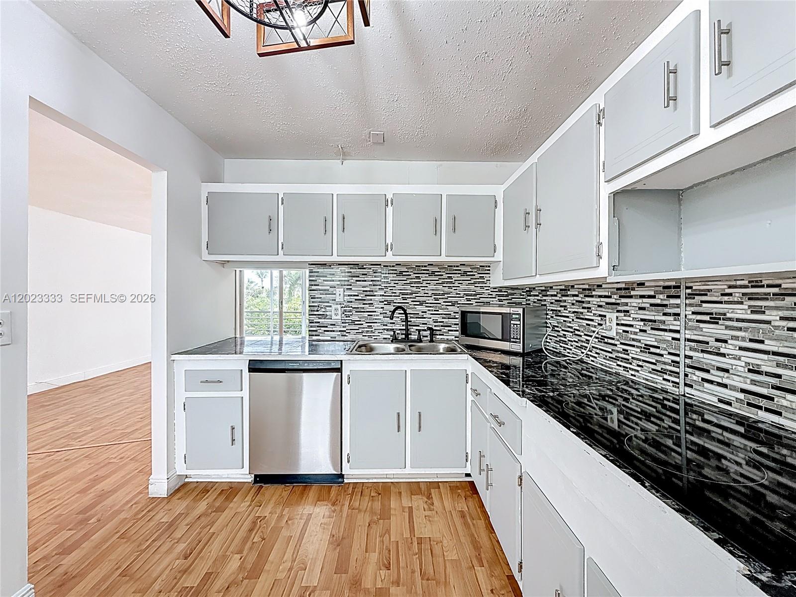 A kitchen features light gray cabinets, black countertops, a mosaic backsplash, and stainless steel appliances — 1000 NE 14th Ave # 411, Hallandale Beach FL 33009, HALLANDALE BEACH, FL