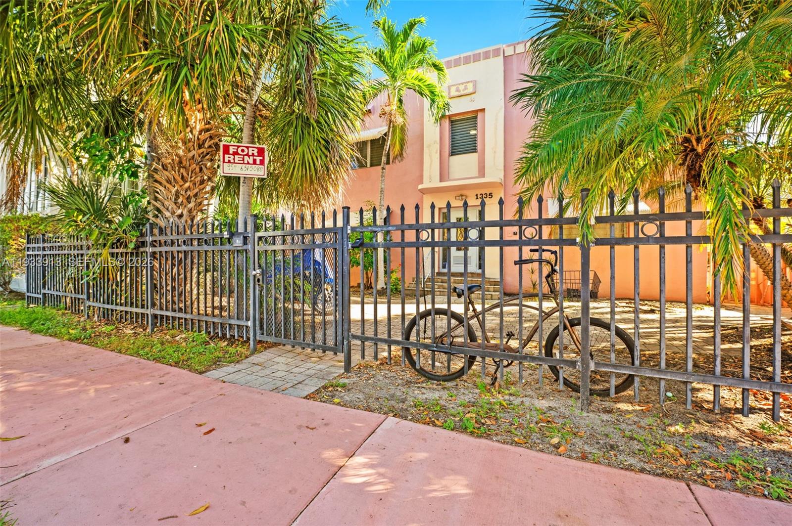 A pink two-story apartment building is viewed from the street behind a black metal fence — 1335 Drexel Ave, Miami Beach FL 33139, MIAMI BEACH, FL