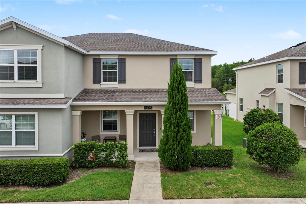 A two-story townhouse with a covered front porch, beige stucco siding, and a small lawn — 3105 AQUA VIRGO LOOP, ORLANDO, FL