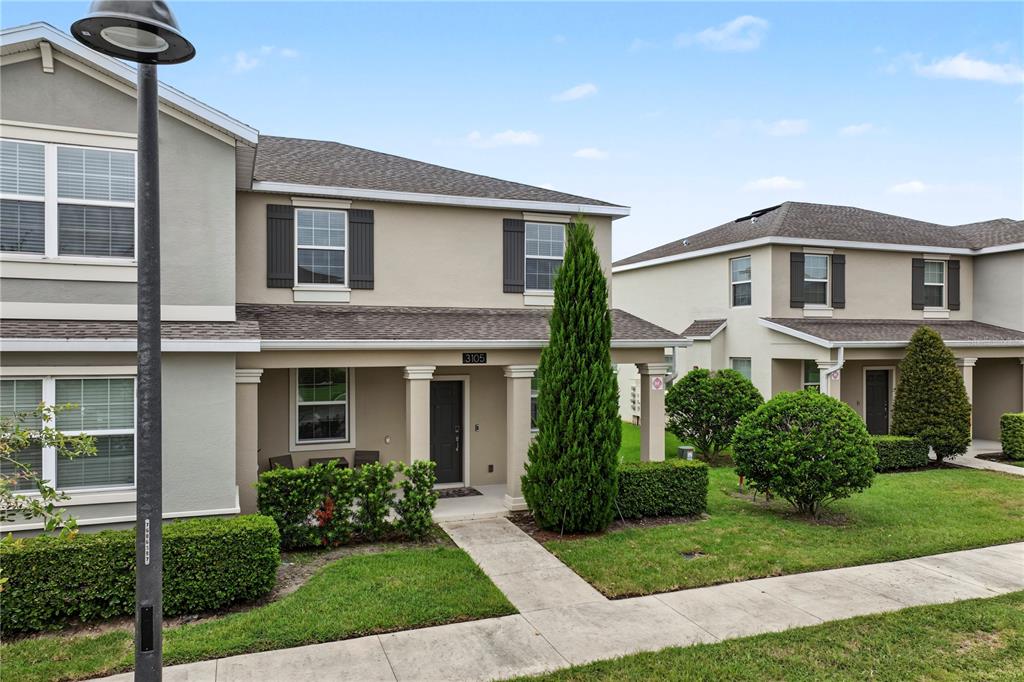 A two-story townhouse exterior features a covered front porch, tan siding, and manicured landscaping — 3105 AQUA VIRGO LOOP, ORLANDO, FL