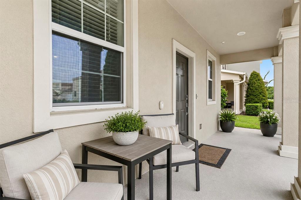 A covered patio features two chairs, a small table, and potted plants near a doorway — 3105 AQUA VIRGO LOOP, ORLANDO, FL