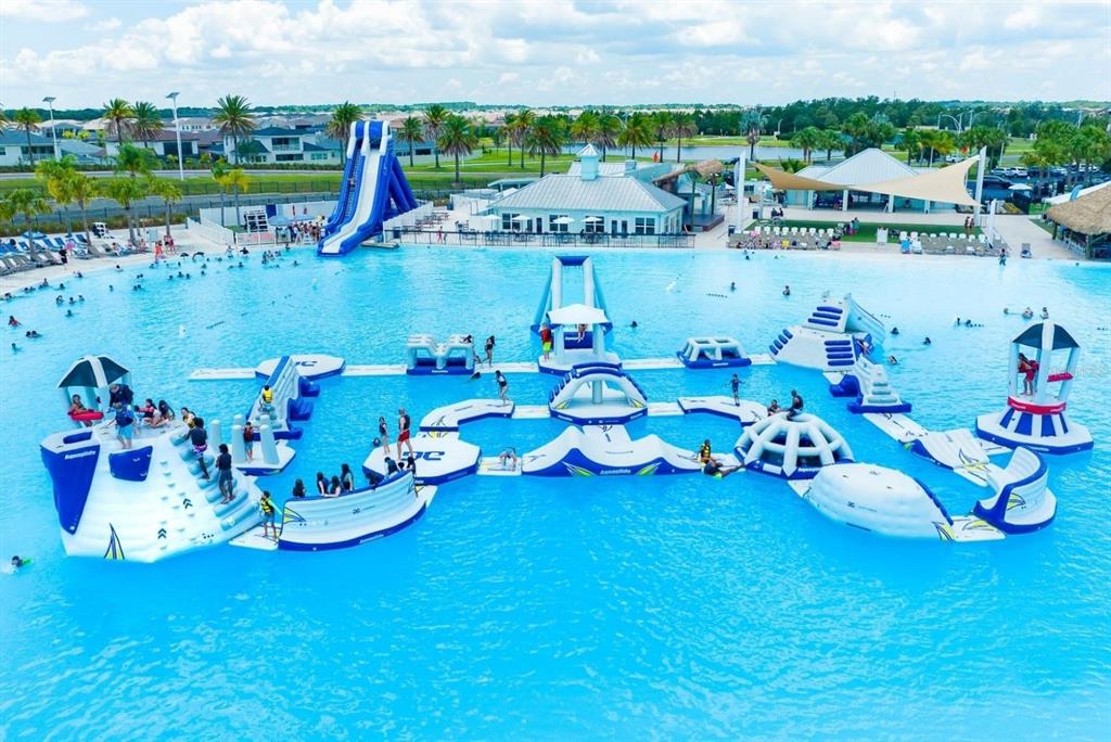An aerial view shows a large swimming lagoon with an inflatable obstacle course and slide — 7566 SEA OAK COURT, PARRISH, FL