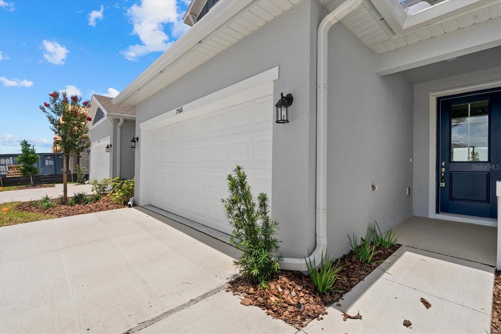 A gray house exterior features a white garage door, a dark blue front door, and landscaping — 7566 SEA OAK COURT, PARRISH, FL