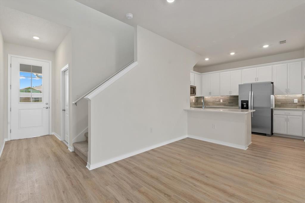 A kitchen with white cabinets and stainless steel appliances sits beside a staircase and entryway — 7566 SEA OAK COURT, PARRISH, FL