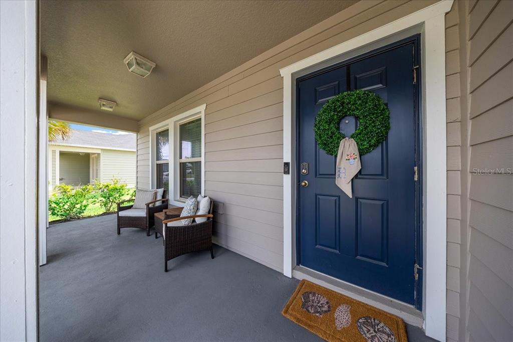 A covered front porch features a dark blue door, two wicker chairs, and a doormat — 9329 SW 57TH TERRACE, OCALA, FL